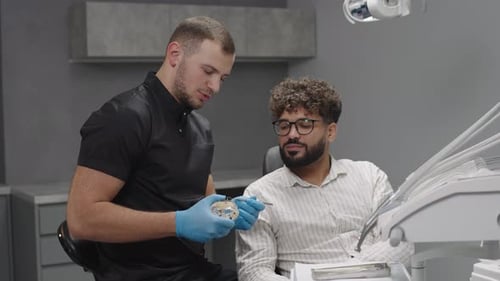 Dentist shows model of tooth to patient in clinic during appointment for oral health care
