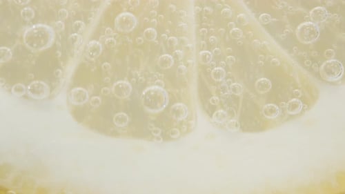 A slice of Lemon in a glass of Soda. Bubbles rise up, macro.