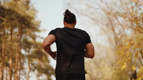 Muscular Athlete in Black Sportswear Close Up Cheerfully Running in a City Park on a Sunny Day Back