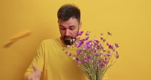 Man with allergies sneezing, holding flowers on yellow