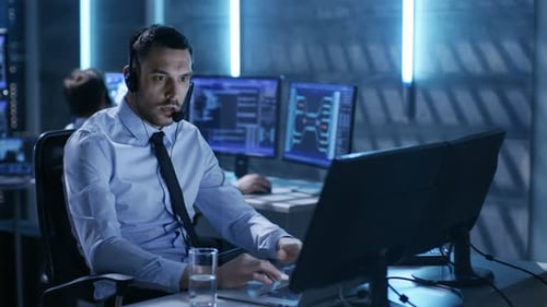 In System Control Center Technical Support Specialist Speaks into Headset while Sitting at His Desk