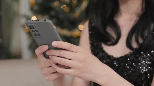 Hands of Young Woman Texting in Smartphone at Christmas Party