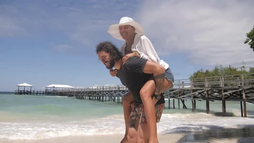 4k video footage of a young man giving his girlfriend a piggyback ride at the beach
