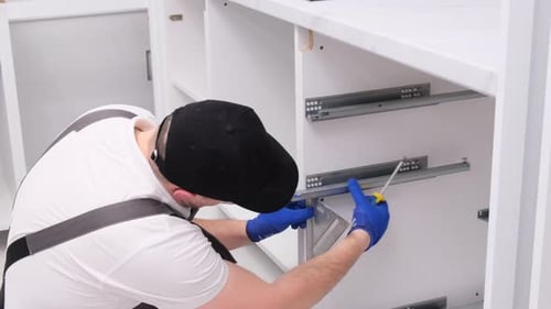 A Man Installs Furniture in the Kitchen with a Screwdriver