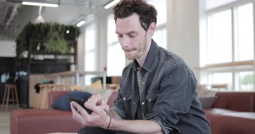 Young adult male using smartphone in a creative office