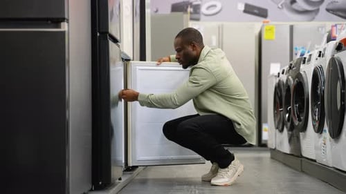 African American Customer Inspecting Refrigerator Freezer Compartment in Appliance Store