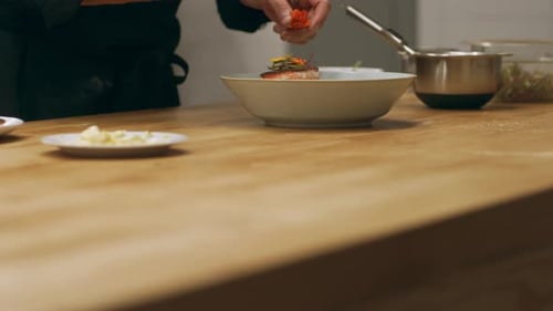 Chef plating salmon dish with floral garnish