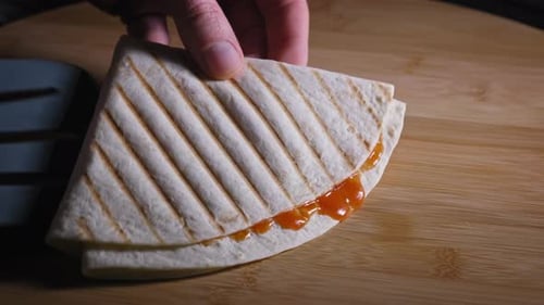 Laying two quarter tortillas with orange sauce on a wooden table (close up)