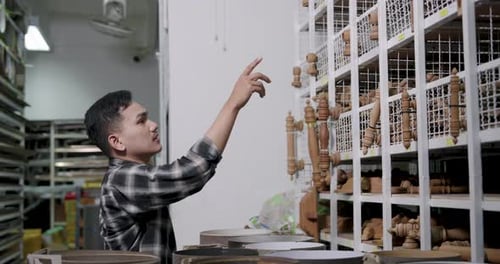 Man Points to Wood Crafts in Indoor Workshop