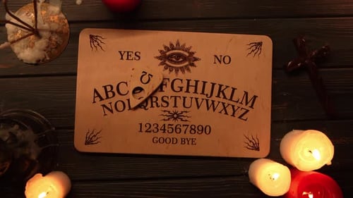 Close Up Video of a Wooden Ouija Board on a Table Surrounded By Candles and a Cross in a Muffed