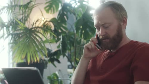 Man Works on Laptop and Talks on Cellphone