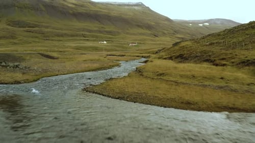Luftaufnahme, Flug über einen kleinen Gebirgsfluss, Berge mit Schnee im Hintergrund.
