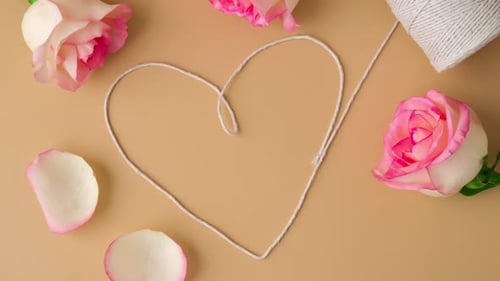 Zoom in Out Tender Pink Roses with Spool of White Cotton Rope in Heart Shape on Beige Background