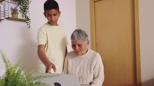 Boy Helping Senior Woman with Laptop Indoors
