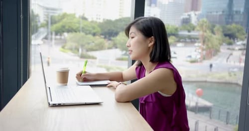 Writing in notebook, woman working on laptop with coffee cup in office