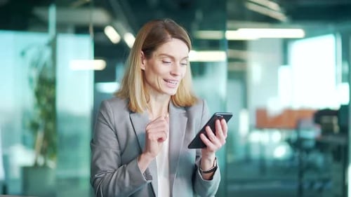 Woman Celebrates Success While Using Smartphone in Office