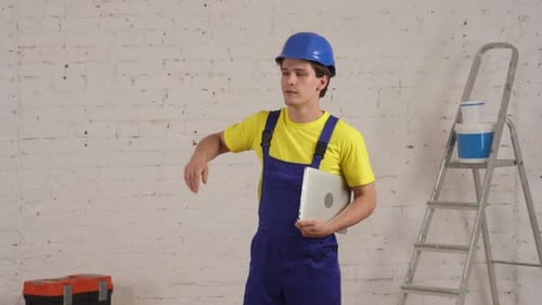 Medium Video of a Young Construction Worker Standing in the Room Holding a Laptop Under His Arm
