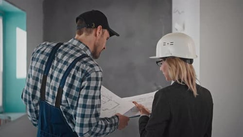 Construction Workers Consult Blueprint in Building Interior