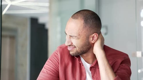 Tired businessman suffering from neck pain while sitting at workplace in a modern business office.
