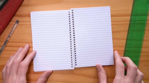 Of A Person Turning The Pages Of A Blank Notebook With Green Ruler And Ballpen On The Side. close up