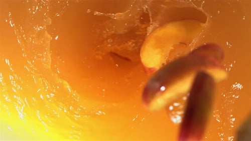 Fruit Slices Plunging into Vibrant Orange Liquid