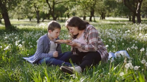 Mutter und Sohn riechen Pizza und genießen das Aroma im Park während des Sommerspaziergangs