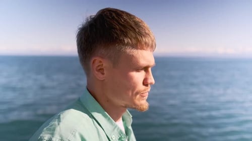 Close Up of Young Blond Man Smiles By the Edge of a Blue Lake