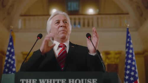 Man Giving Speech Behind Podium With Flags