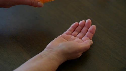 Close Up Footage of Elderly Hands Pouring Pills From an Orange Prescription Bottle Into the Palm