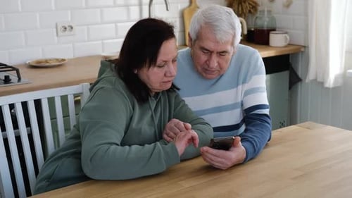 Mature Couple Using Cell Phone in Kitchen Together