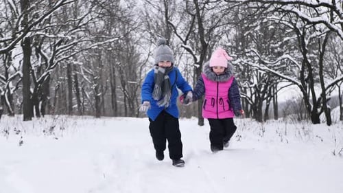 Niños: un niño y una niña se toman de la mano y corren en invierno en el bosque