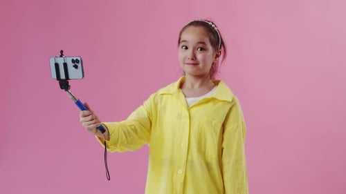 Girl Holds Phone on Selfie Stick Against Pink Background
