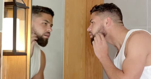 Bartpflege, Mann untersucht Spiegelbild im Badezimmerspiegel zu Hause