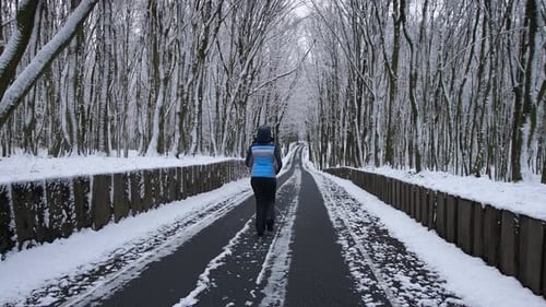 A Woman Runs Along the Road in the Middle of the Forest The Trees are Covered with Snow on the Way