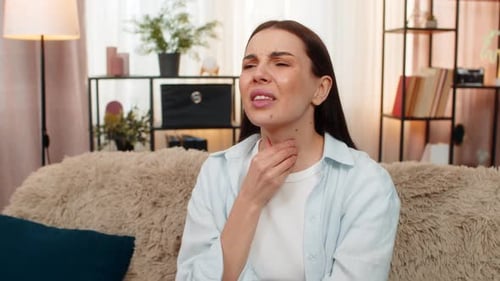 Young Woman on Sofa Holding Throat Coughing Painfully Feeling Sick Unhealthy Experiencing Flu