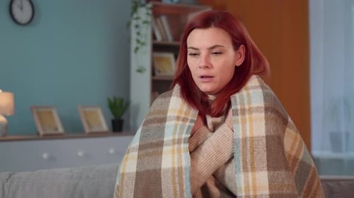 Portrait of a Young Woman in a Warm Blanket Warming Herself at Home Sitting on Sofa Looking at
