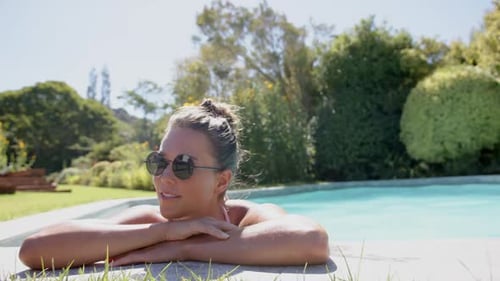 Relaxing by pool, woman wearing sunglasses and leaning on edge, enjoying sunny day, copy space