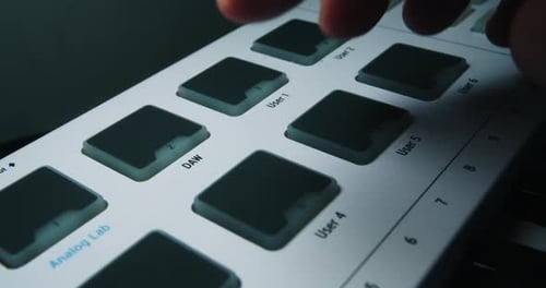 A musician producer presses pads and buttons on a midi keyboard to record a song in his music studio