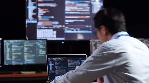 Close Up Back View Of Asian Male Programmer Walking Into The Working Space To Write Code By A Laptop