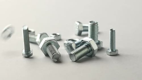 Metallschrauben und Sechskantmuttern fallen auf grauen Hintergrund, Nahaufnahme