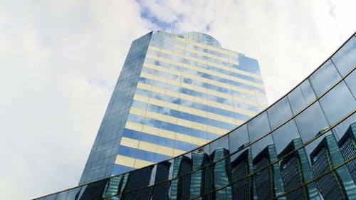 Low angle dolly forward of a beautiful, sleek, corporate skyscraper that reflects a vibrant blue sky