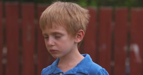 Child in Blue Shirt Looking Sad by Fence