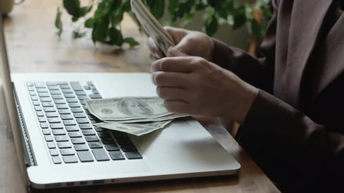 Business Woman Counting Dollar Bills Sitting at Desk in Office