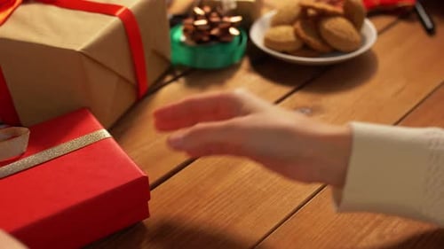Hands placing Christmas gifts on a wooden table