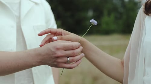 Engaged Couple Touching Hands with Flower Outside