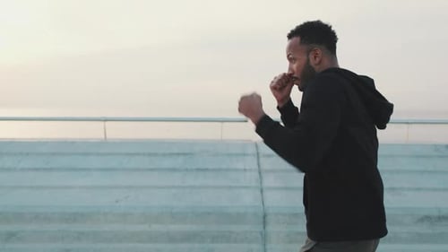 Young athlete boxer practicing punching technique while standing on the embankment