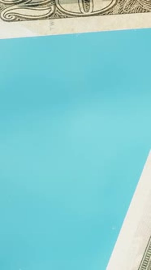 Vertical video. I throw twenty-dollar bills onto a glass table. On a blue background. Low angle view