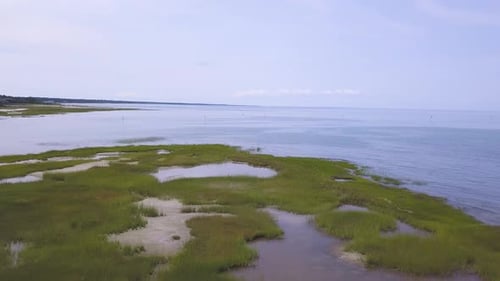 The camera pans from right to left in front of the dune grass, and tidal pools. A kayaker can be see