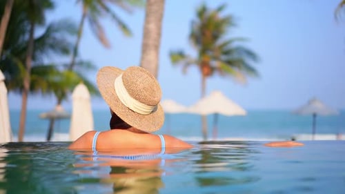 Back of a woman in the swimming pool of a tropical hotel in Miami, blurred umbrellas and sea on back