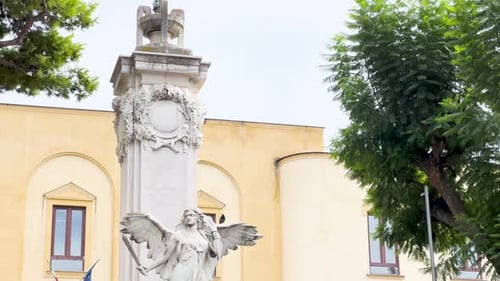 A marble angel statue with spread wings stands in front of a historic building, symbolizing peace or